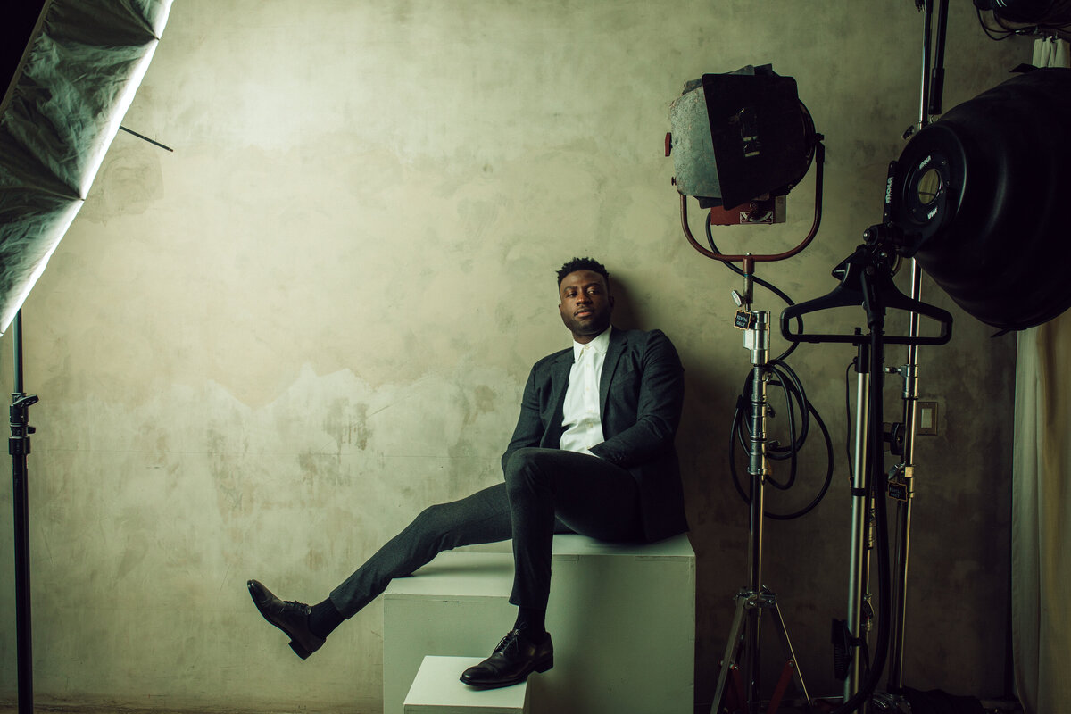 Portrait Photo Of Young Black Man In Suit Leaning Against The Wall While Seated In a White Box Los Angeles