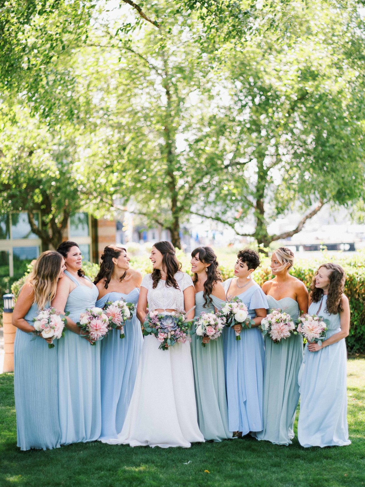 Our Beautiful bride and her maids wearing light blue dresses and holding greenery bouquets, smiling in the sunshine