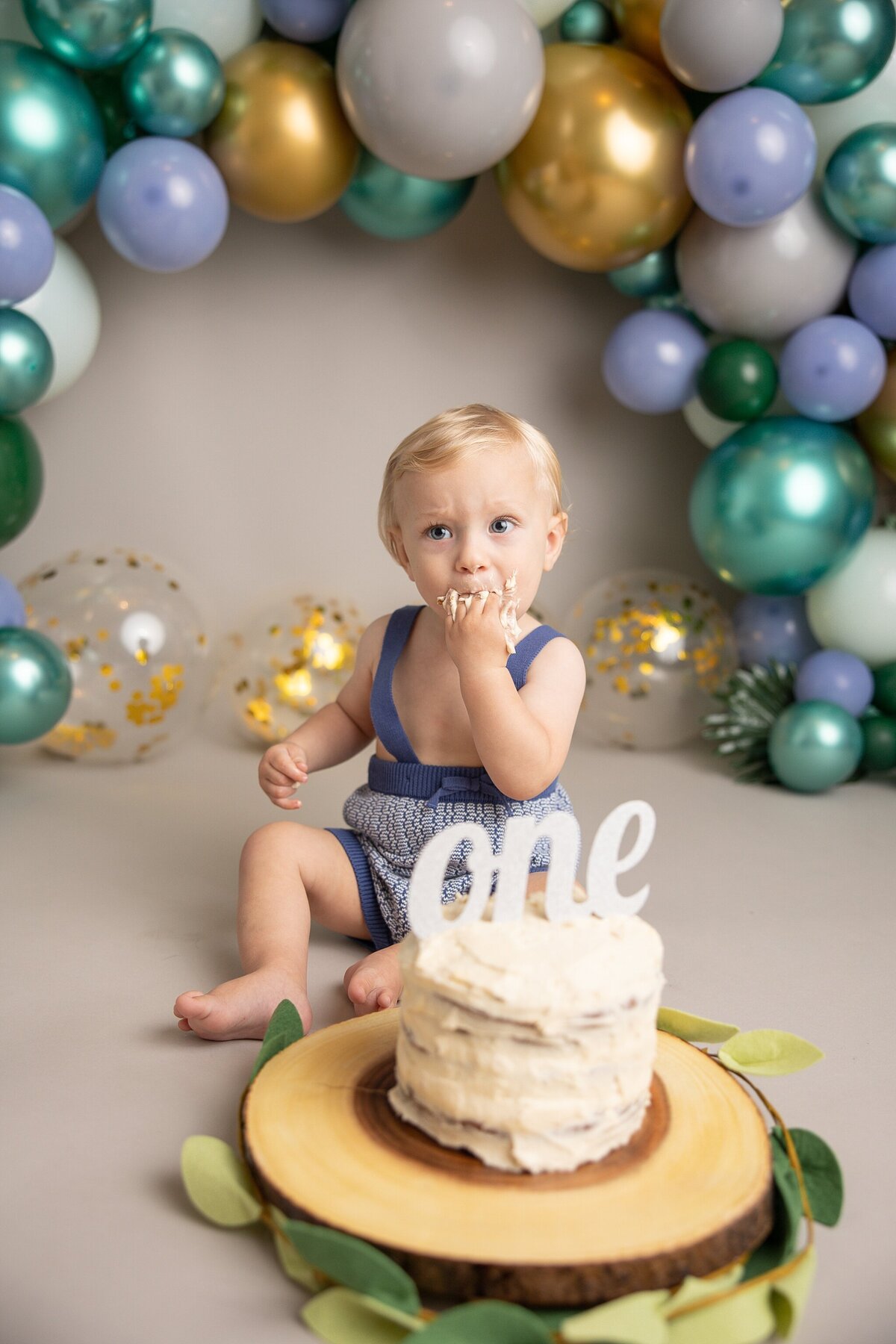 baby boy with one cake sitting looking to the left while he tastes the cake in portland area studio for his first birthday