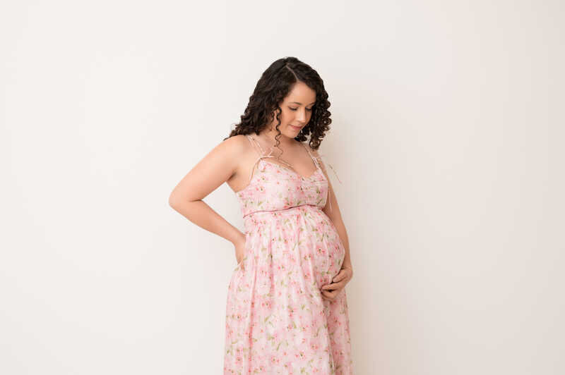 Expecting mother in soft pink dress holding her baby bump during Houston maternity photoshoot.