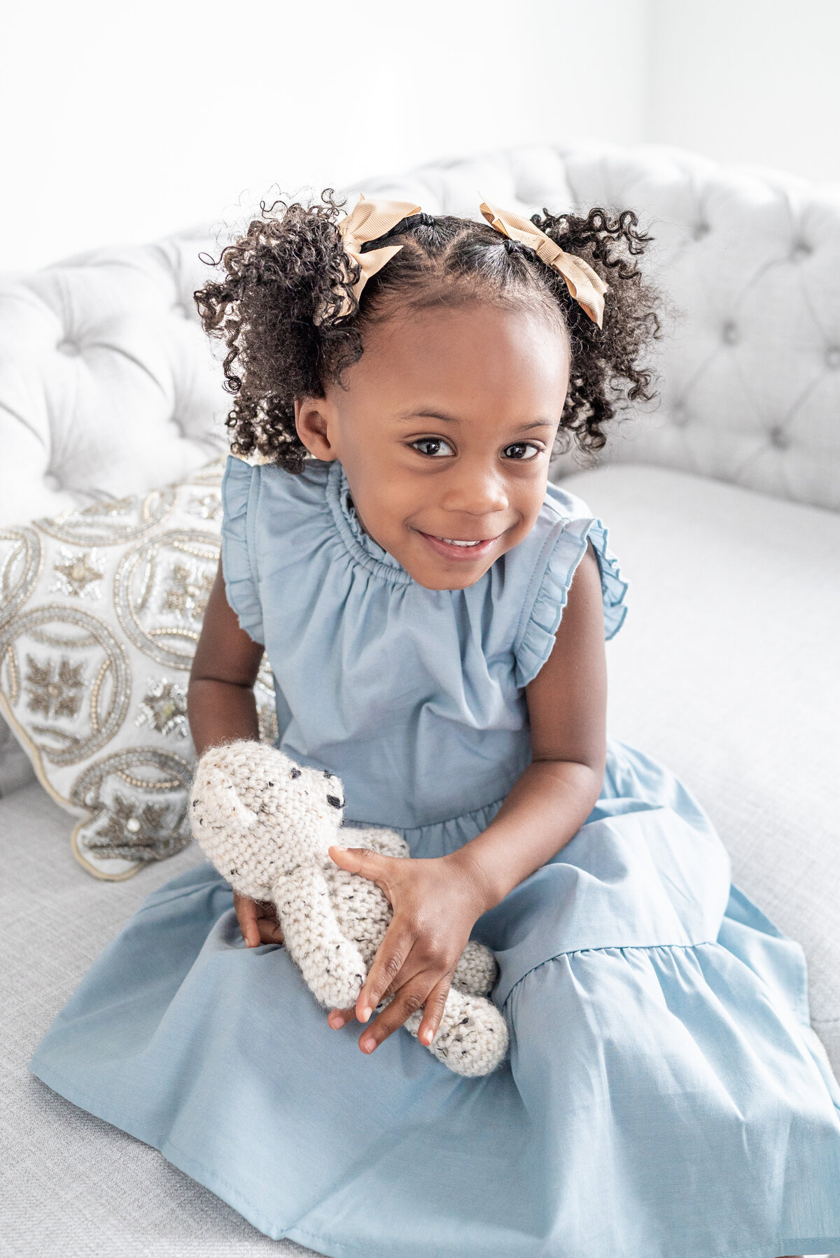 A little girl holding a teddy bear  smiles at the camera in a studio in Hampton Cove