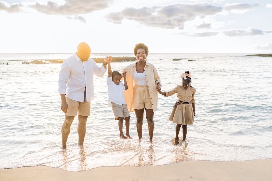 Family standing in the water, dressed in khaki white and peach. Family is dressed really nice. 