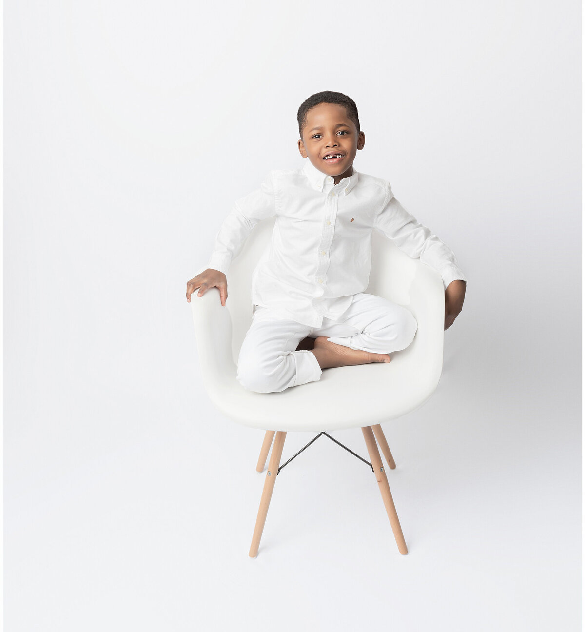 A boy sitting on a white chair  wearing a trendy outfit .