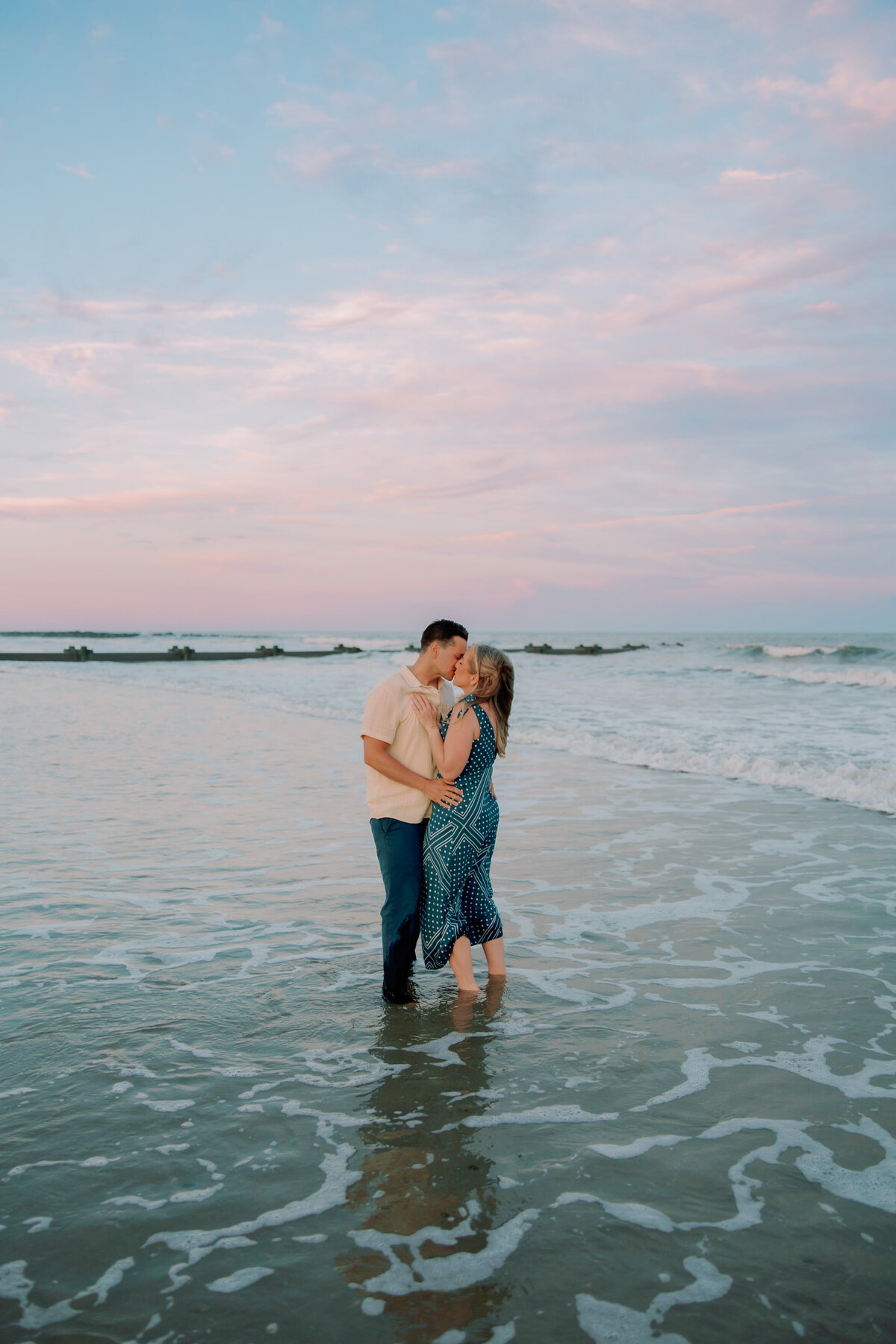 A couple kissing as they stand ankle deep in the ocean 