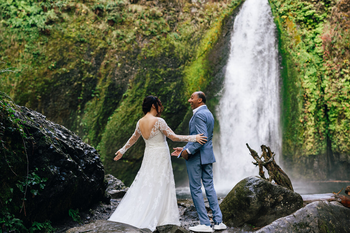 A bride and groom share a first look at the base of a beautiful waterfall at their Oregon elopement.