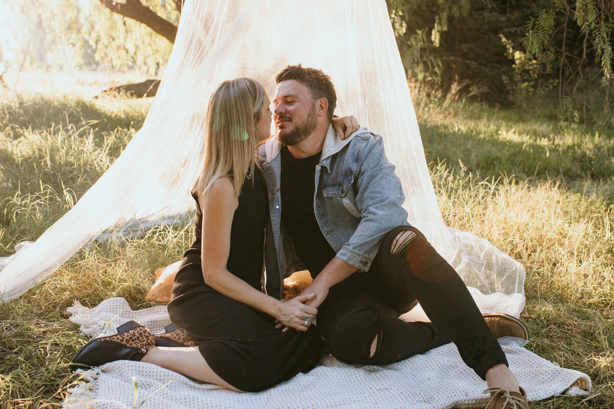 Romantic moment between a couple sitting on the grass staring into each other's eyes while the sunsets behind them. 