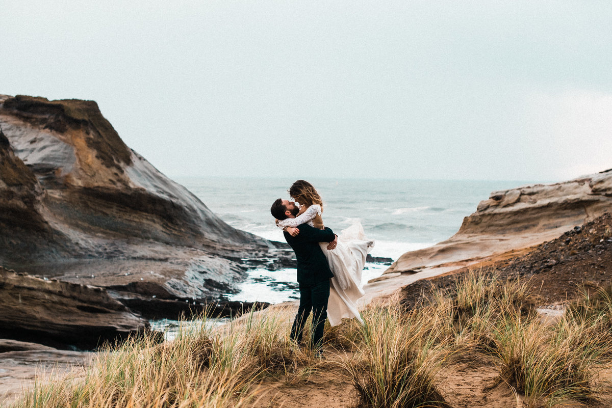 Groom hugging and lifting bride on seaside cliffs near Cape Kiwanda in Oregon!