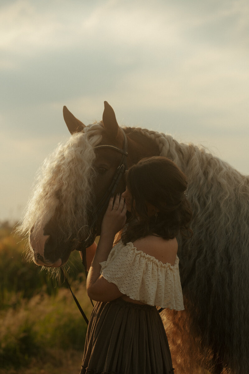Een dromerige, filmische paardenfoto waarin een vrouw haar paard fluisterend omarmt, vastgelegd in warm licht en met een mysterieuze achtergrond.