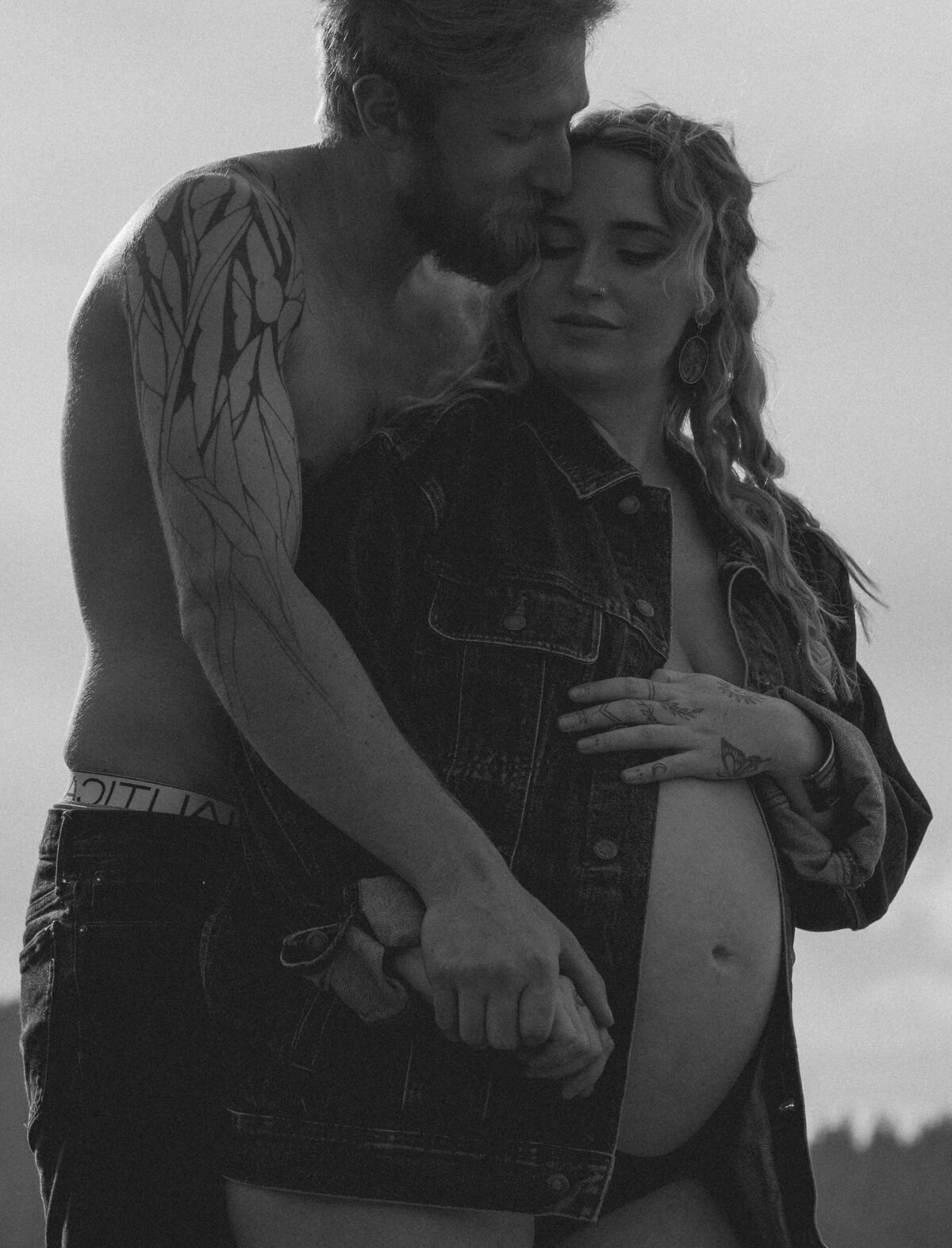 maternity photo of woman standing with her partner, softly embracing and holding hands