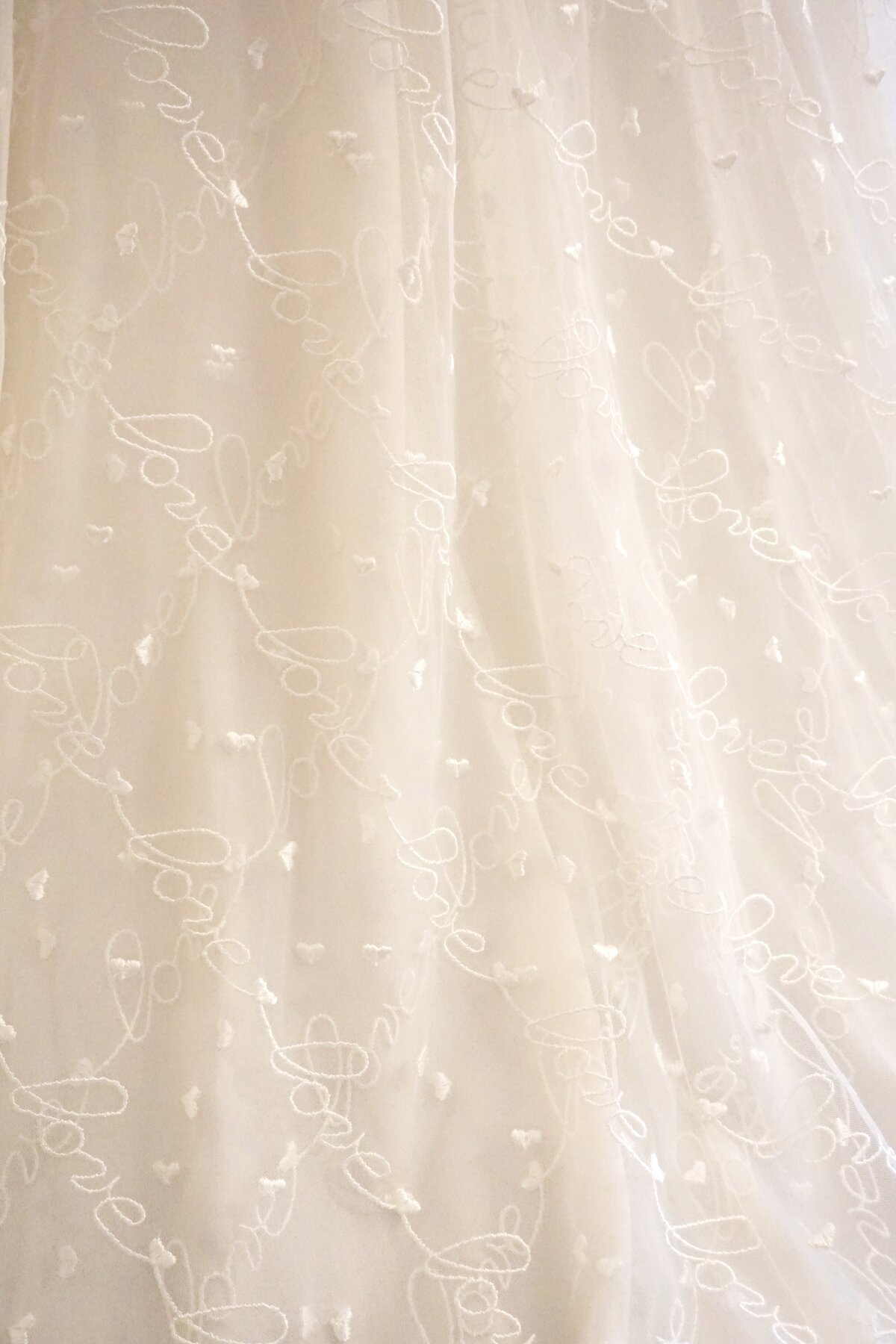 The criss-crossing layers of tulle on the Norma Jean wedding dress style are embroidered with lines of hearts and the word "love."