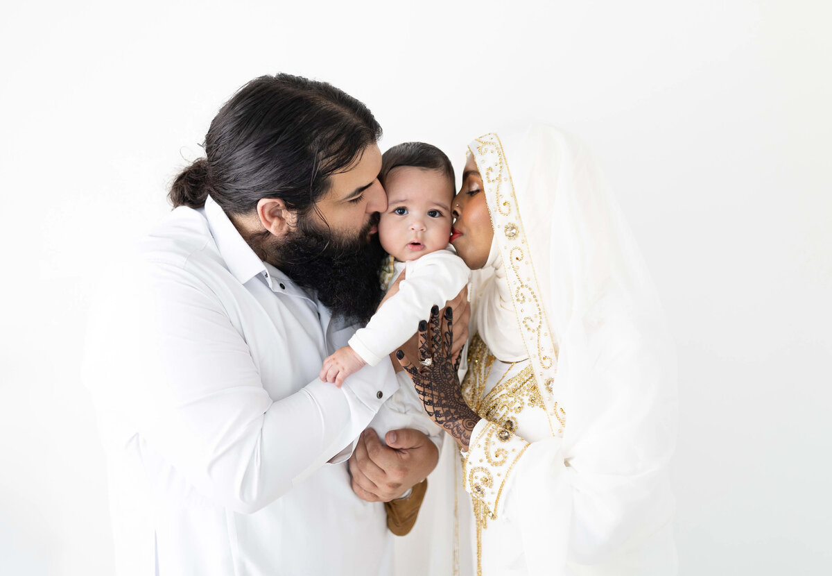 Mom and dad kissing baby i n white outfits - cultural newborn session in Minneapolis area
