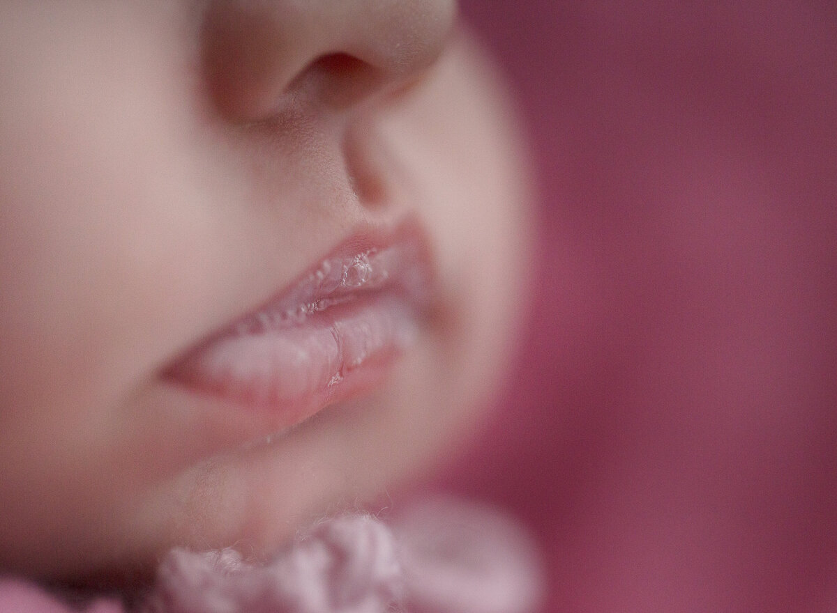 close up of newborn baby girls lips in a pink background