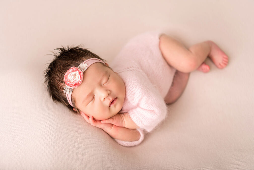 Connecticut newborn photographer creates adorable posed portrait of smiling baby girl wrapped in pink with floral headband on neutral backdrop