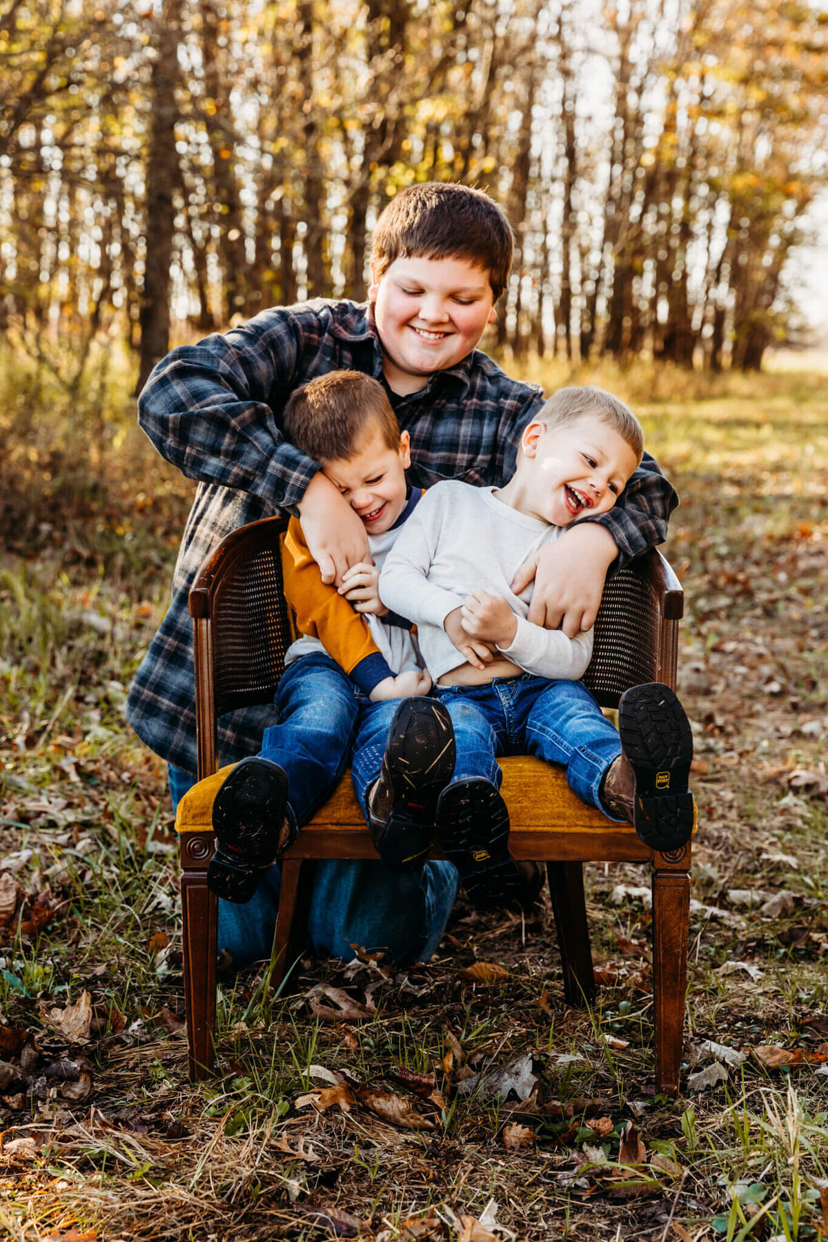 3 brothers tickling each other while sitting in a chair in a field near Oshkosh.