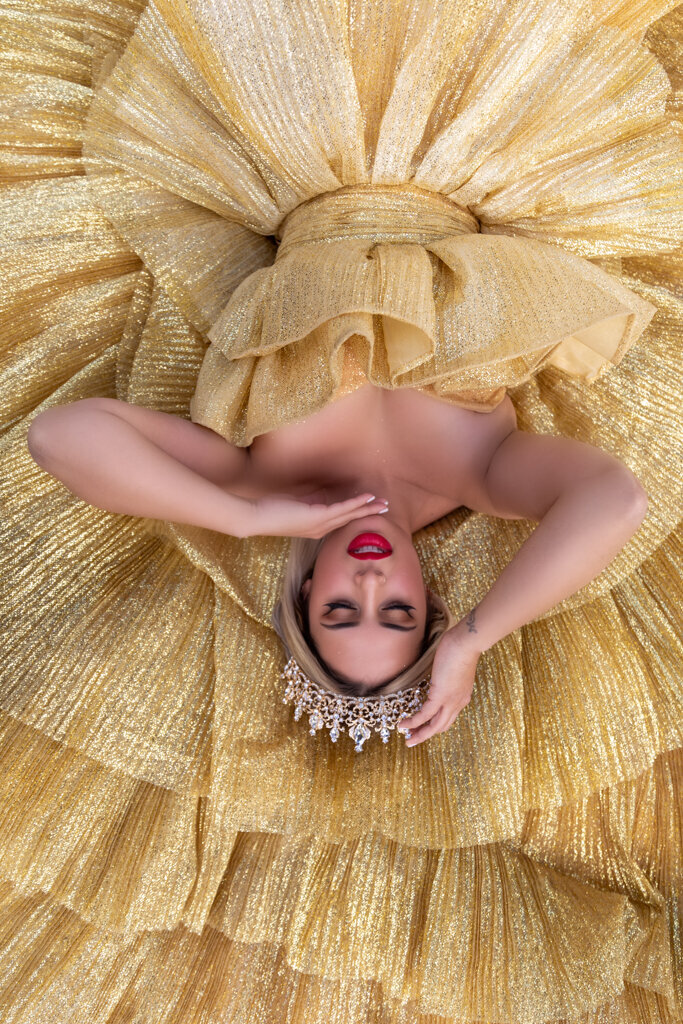 Elegant portrait session with blonde woman wearing crown laying on golden princess ball gown