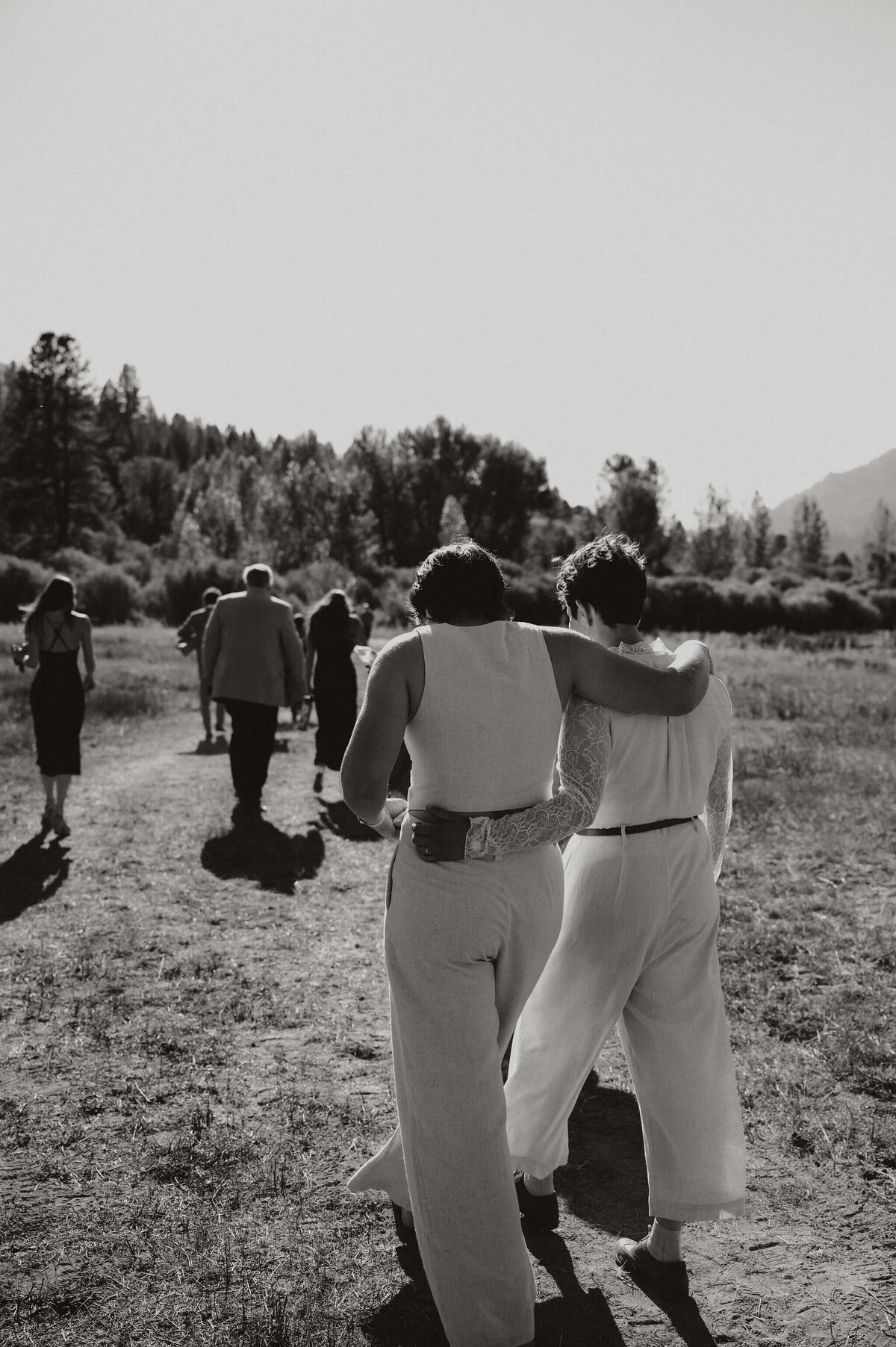 Couple with arms around each other walking with their wedding guests outdoors.