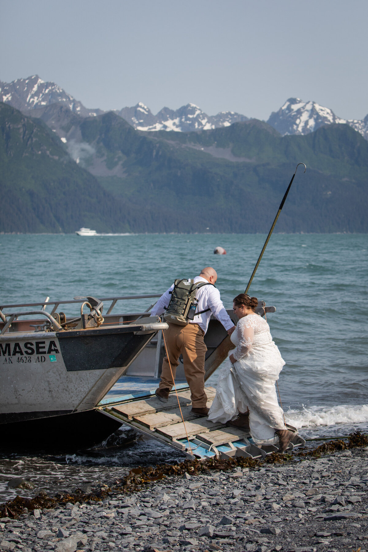 A groom reaches out to help his bride climb onto a boat in Alaska.
