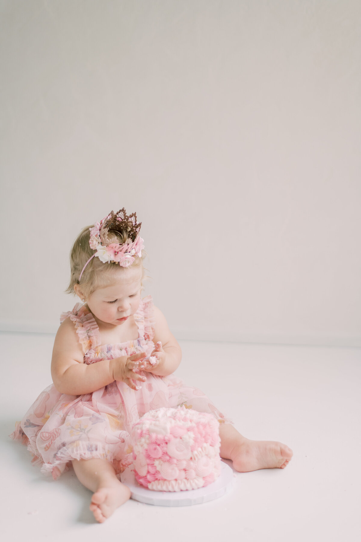 Little girl playing with cake on fingers for her first birthday caske smash in Burlington