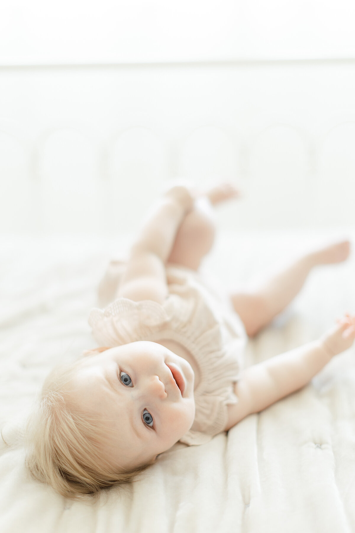 A baby girl rolling around on a bed at a DFW photography studio for her milestone portraits.