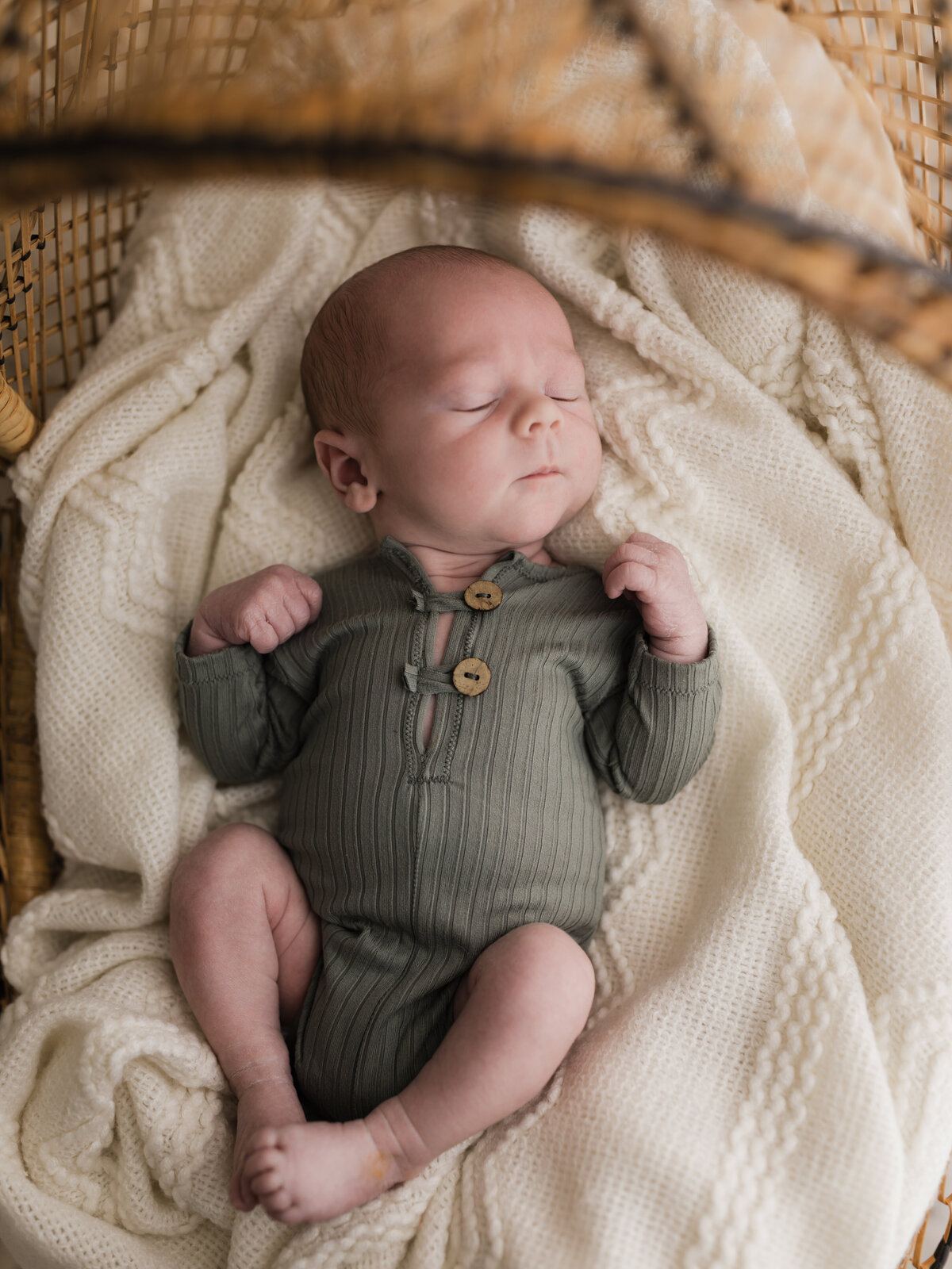 newborn baby boy in green onesie laying in bassinet