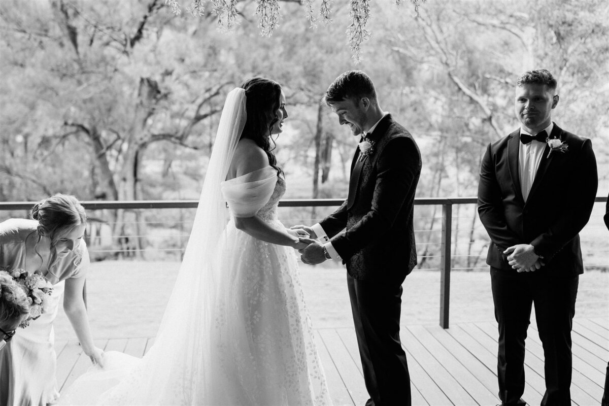 A radiant bride, adorned in ivory lace, clasps hands with her groom under a cascading arch of roses as vows intertwine their destinies.