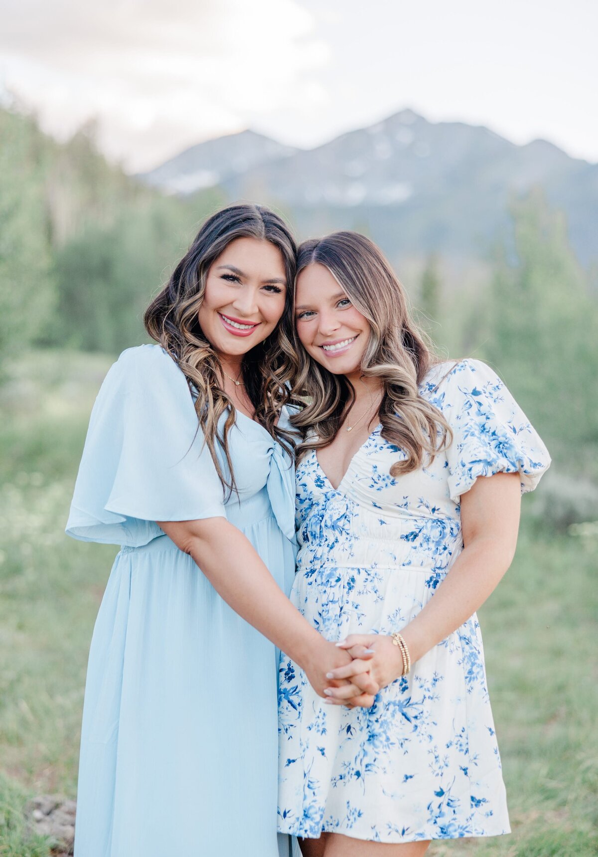 Smiling sisters in blue dresses hold hands while snuggling in a field