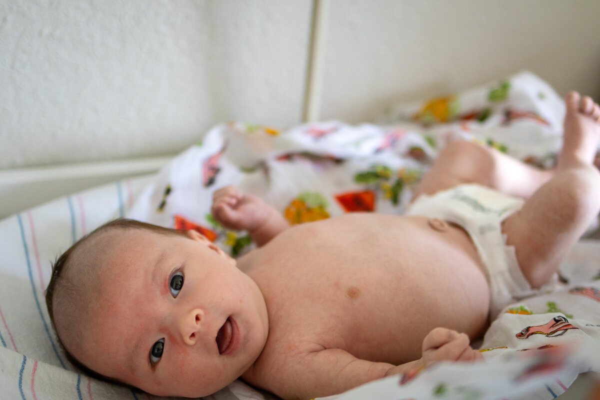 A bright-eyed newborn lying on a playful, colorful blanket during an in-home lifestyle session by San Francisco newborn photographer.