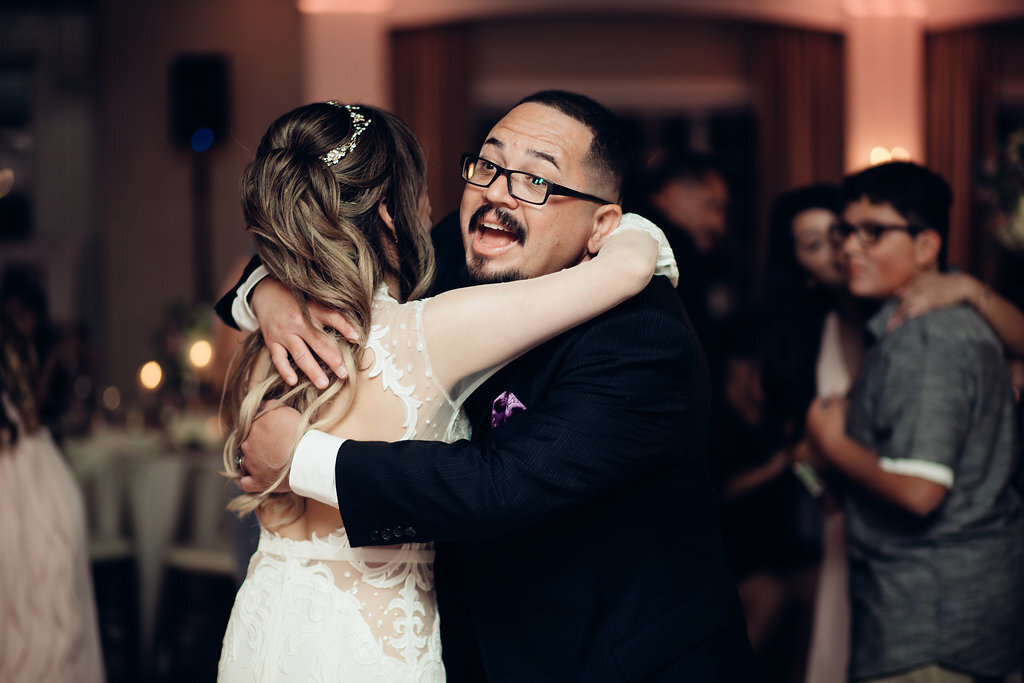 Wedding Photograph Of Man In Black Suit With Eye Glasses Hugging The Bride Los Angeles