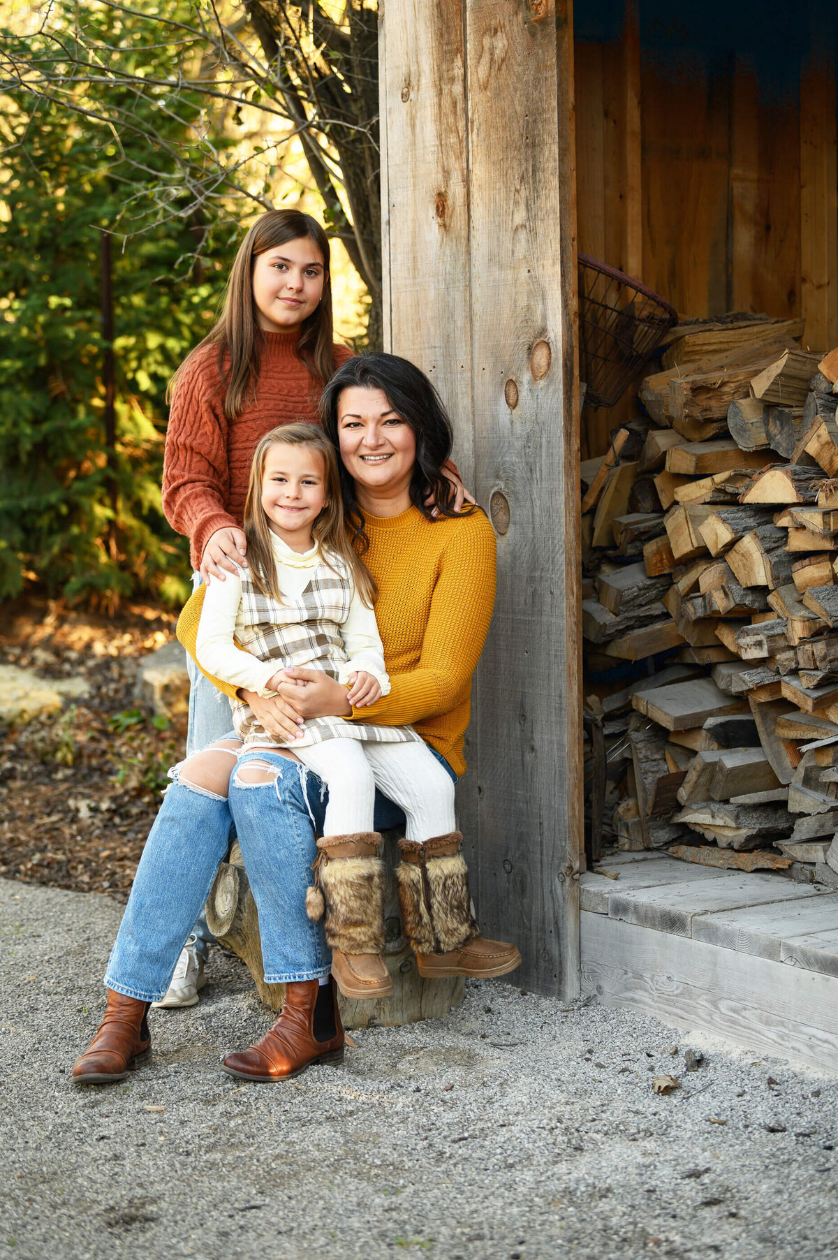 Mom wearing a yellow shirt with her two daughters near a wood shed for their fall family photos in Burlington, ON