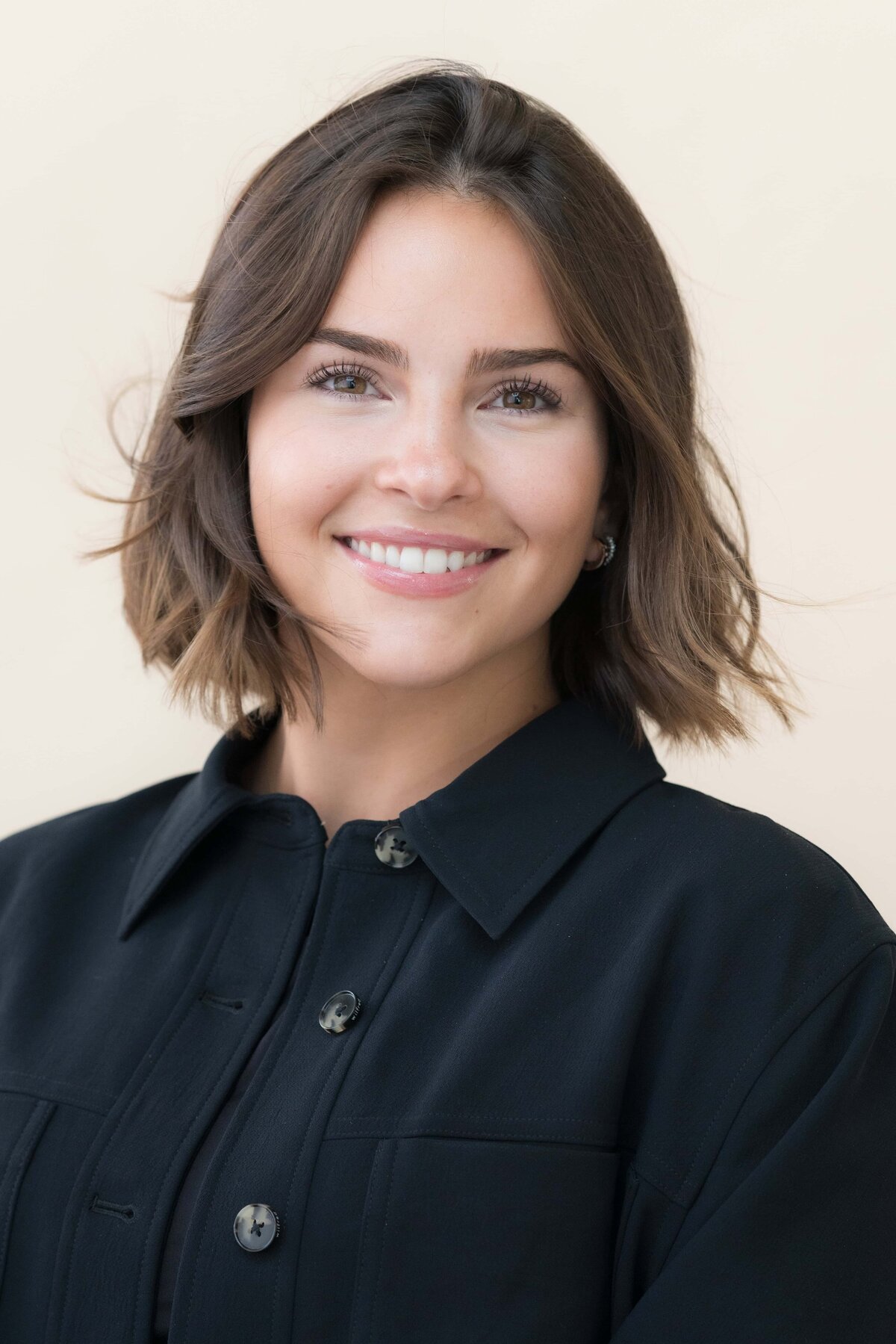 young woman with dark hair smiling while wearing a dark shirt posed for a modeling headshot