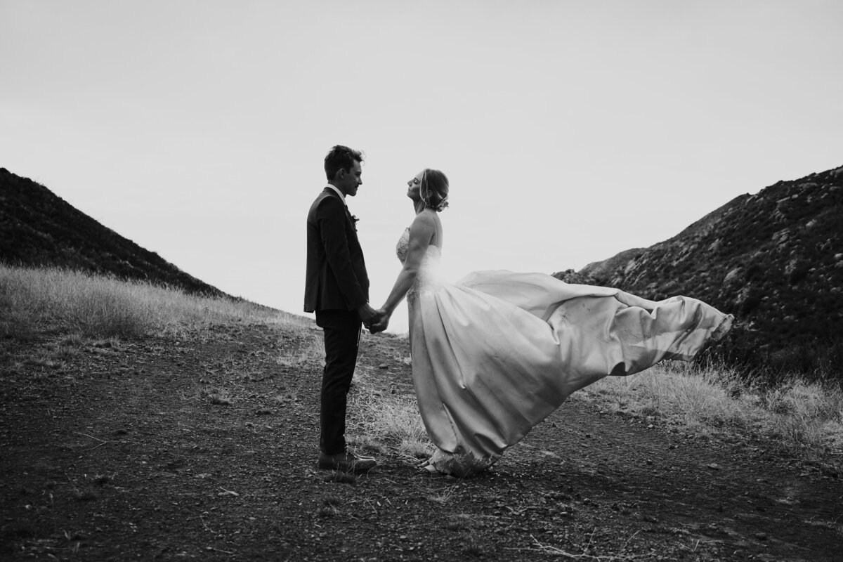Bride and groom stand facing each other during sunset as her gown blows in the wind