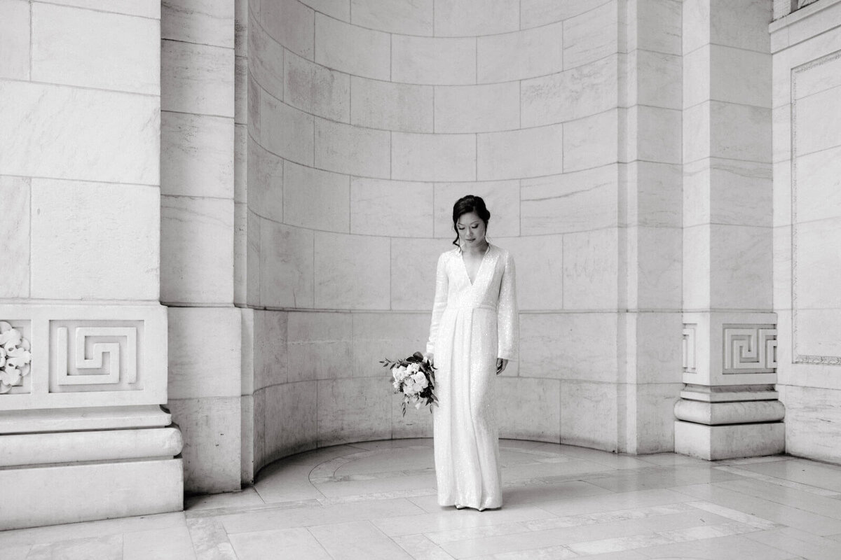 The bride is looking down the marble floors, inside the classic New York Public Library, NYC. Image by Jenny Fu Studio