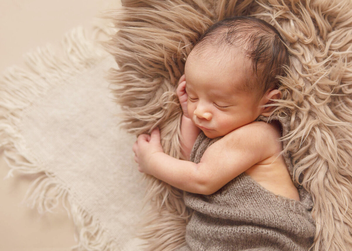 Little boy dressed in grey romper asleep on a newborn bed
