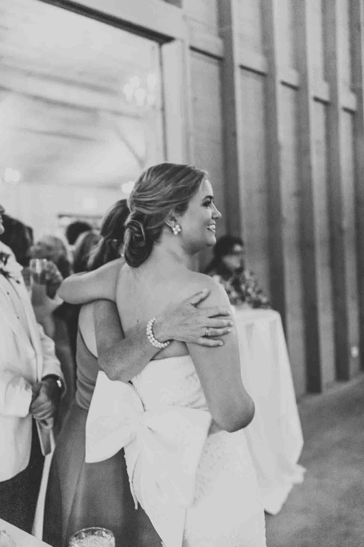 bride is being hugged by mom as she watches her husband dance with his mom.