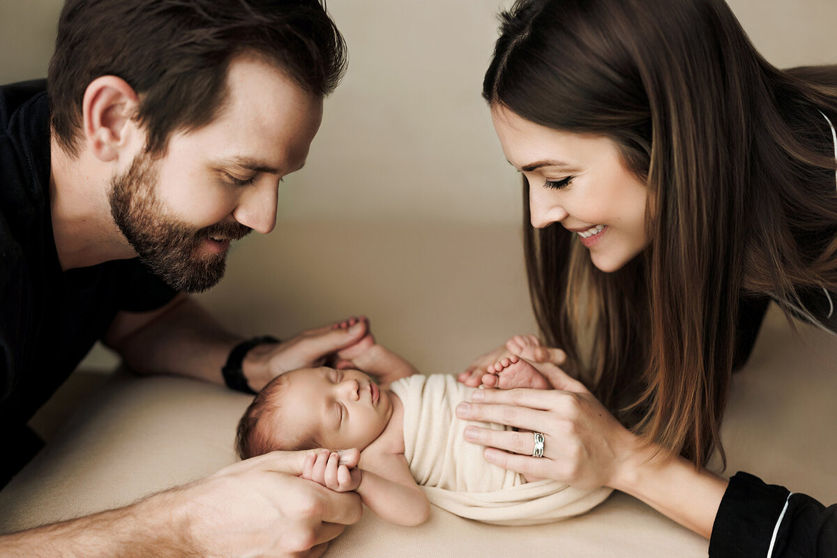 Beautiful mom and dad with newborn baby boy smiling down at him