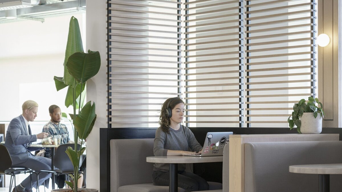 Office nook with built-in banquette featuring grey fabric upholstered seats,  wooden tables and slatted screens
