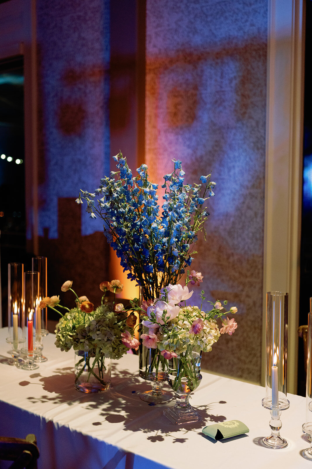 Glass vases filled with vibrant orange and pink flowers and glowing votive candles arranged on tiered wooden shelves at Callie & Hayes’ Burritt on the Mountain wedding reception.