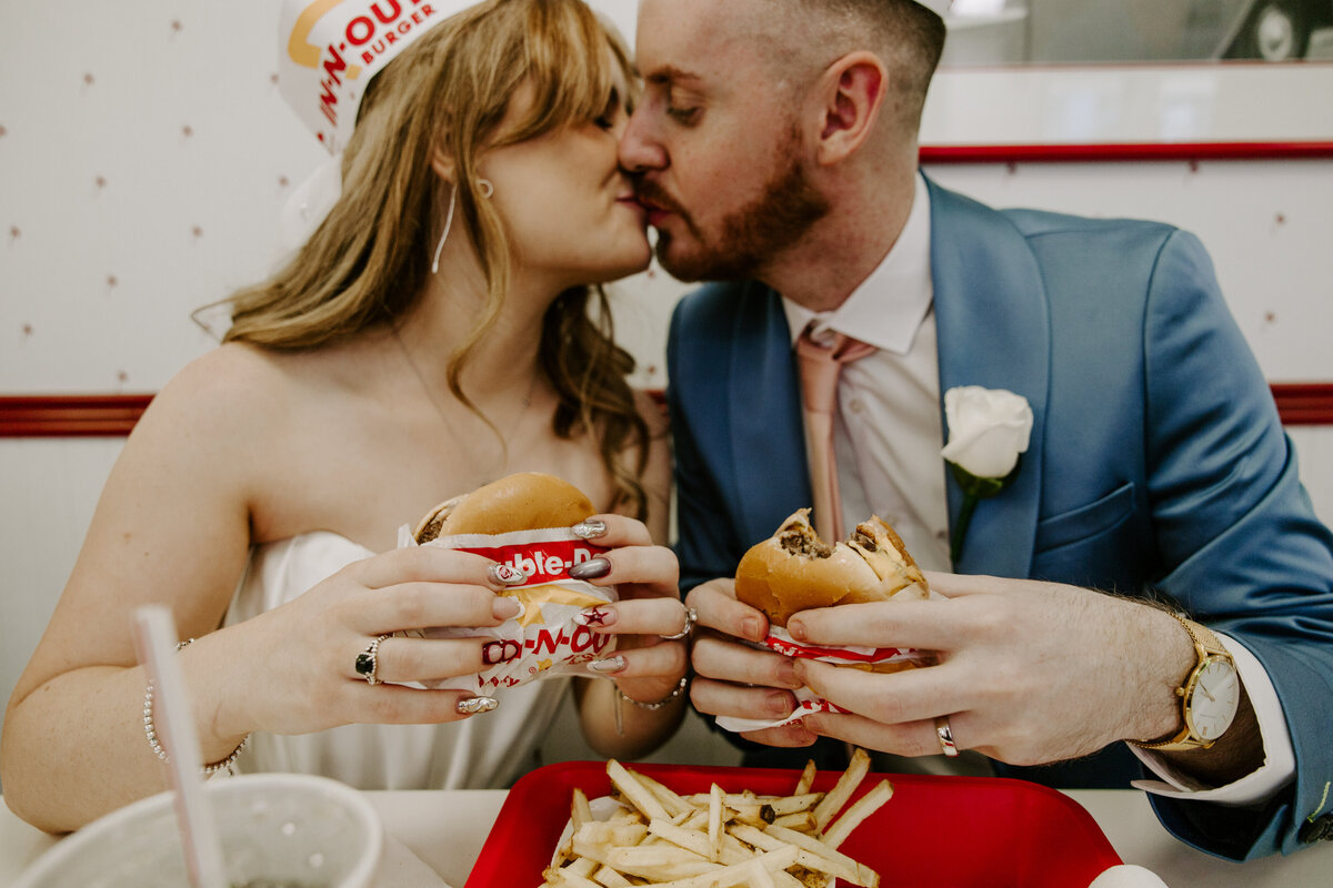 A couple leans in for a kiss while holding In-N-Out burgers.