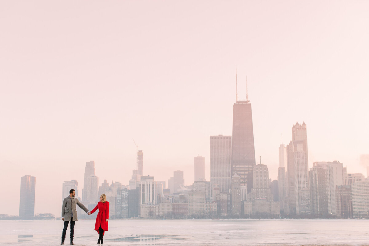 An engagement photo in front of a frozen Lake Michigan with the Chicago skyline in the background.