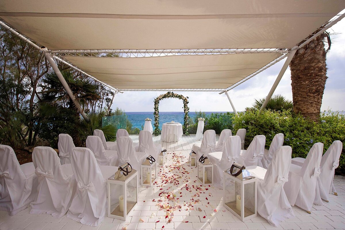 Petals decorate the aisle between chairs covered in white linen leadning towards a floral ceremony arch