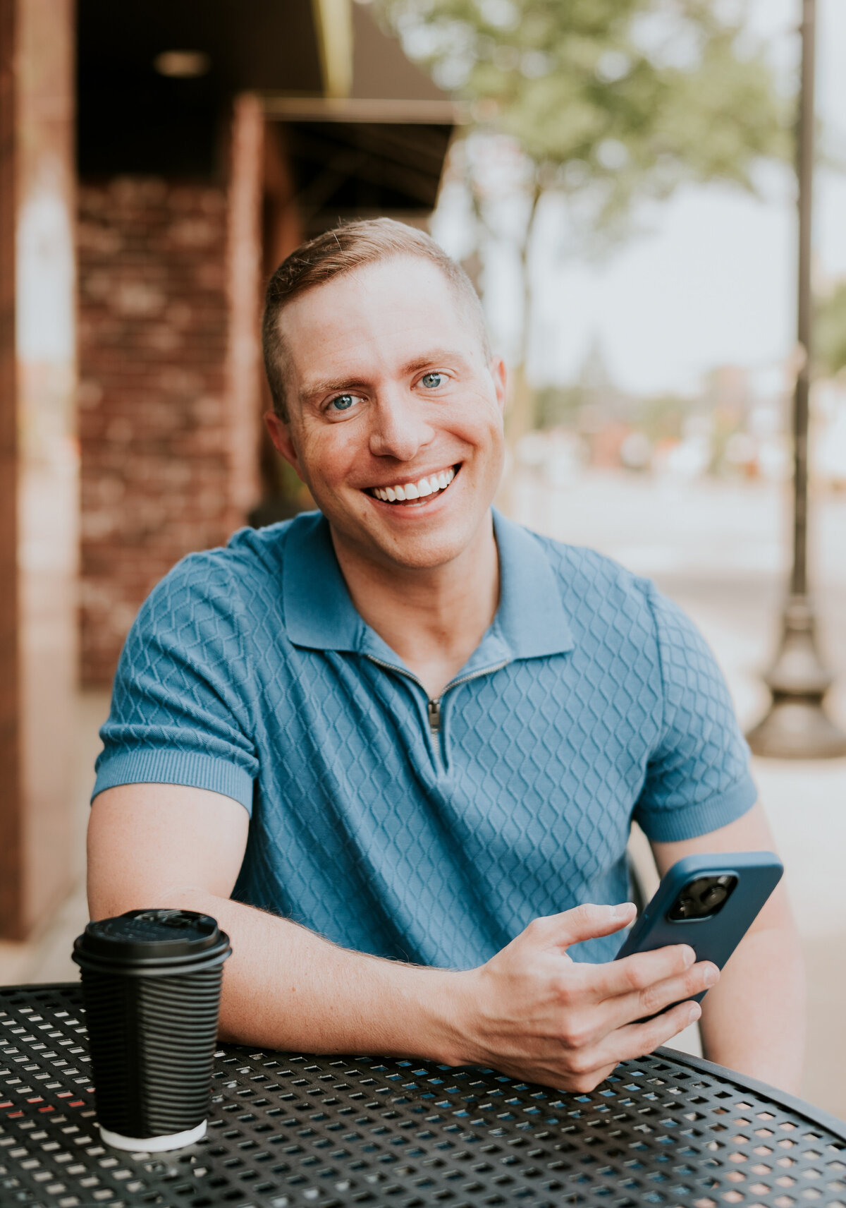 Brandon smiling confidently with coffee and phone in downtown Minneapolis, captured by Shannon Kathleen Photography for online dating profile