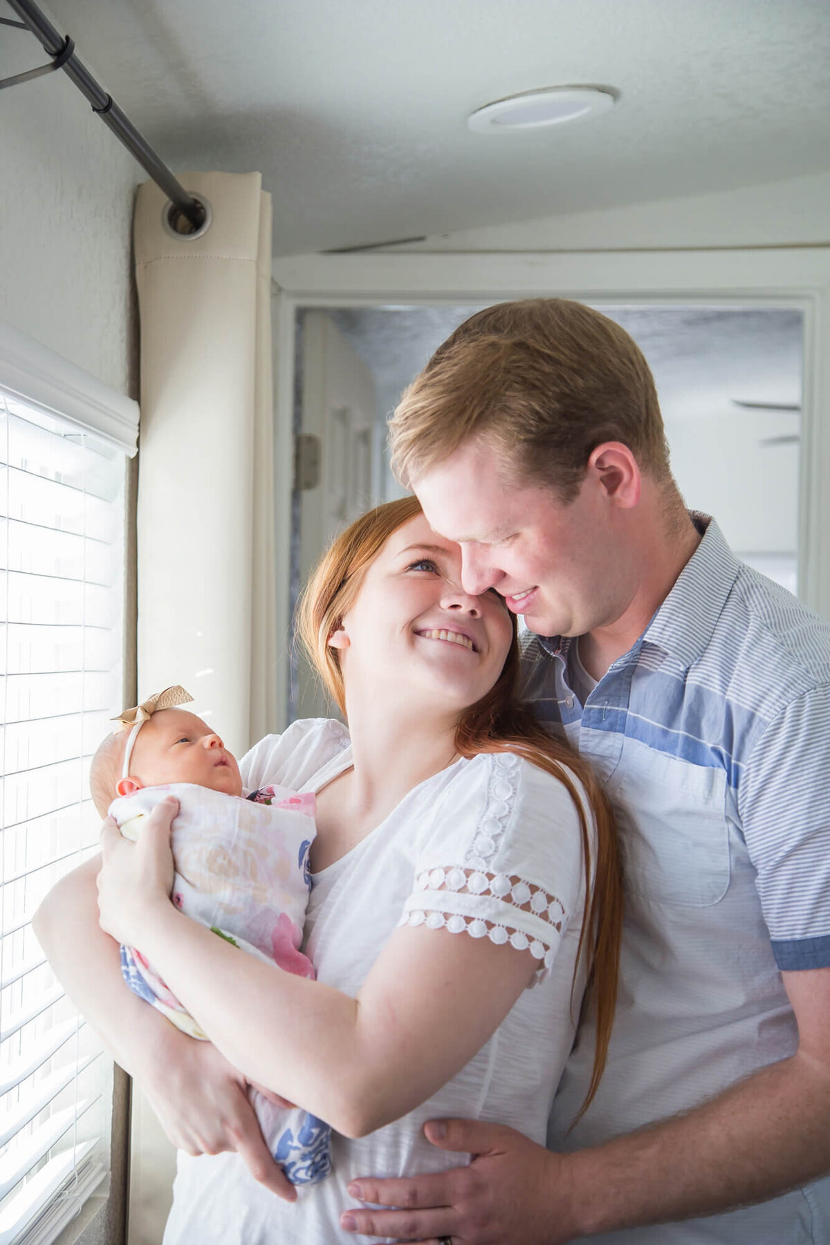 Couple holding newborn baby girl and looking at each other at their lifestyl in home newborn session