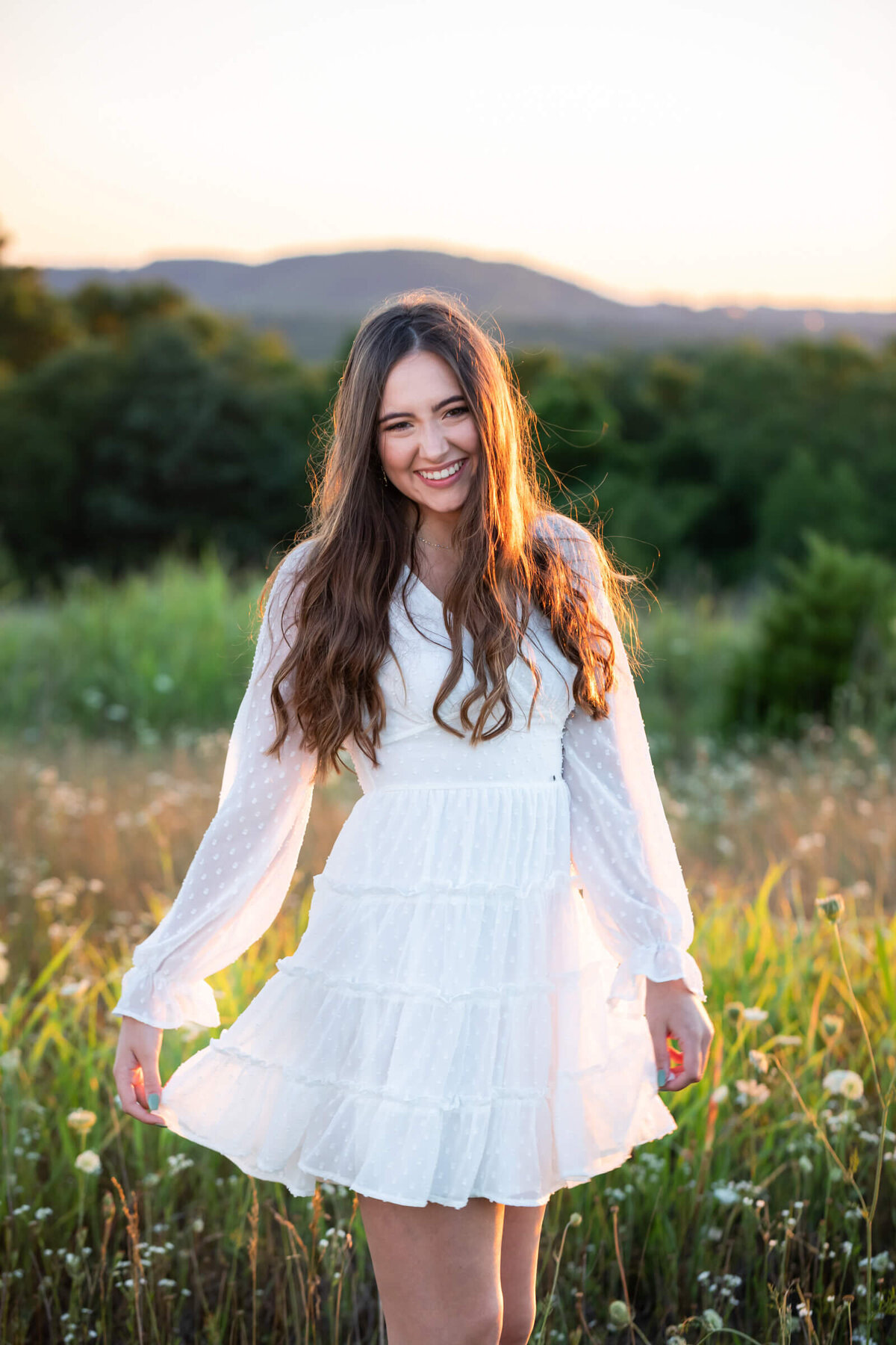 A lovely teen girl wearing a boho style white dress twirls and laughs in a wildflower field. Photograph by Dynae Levingston.