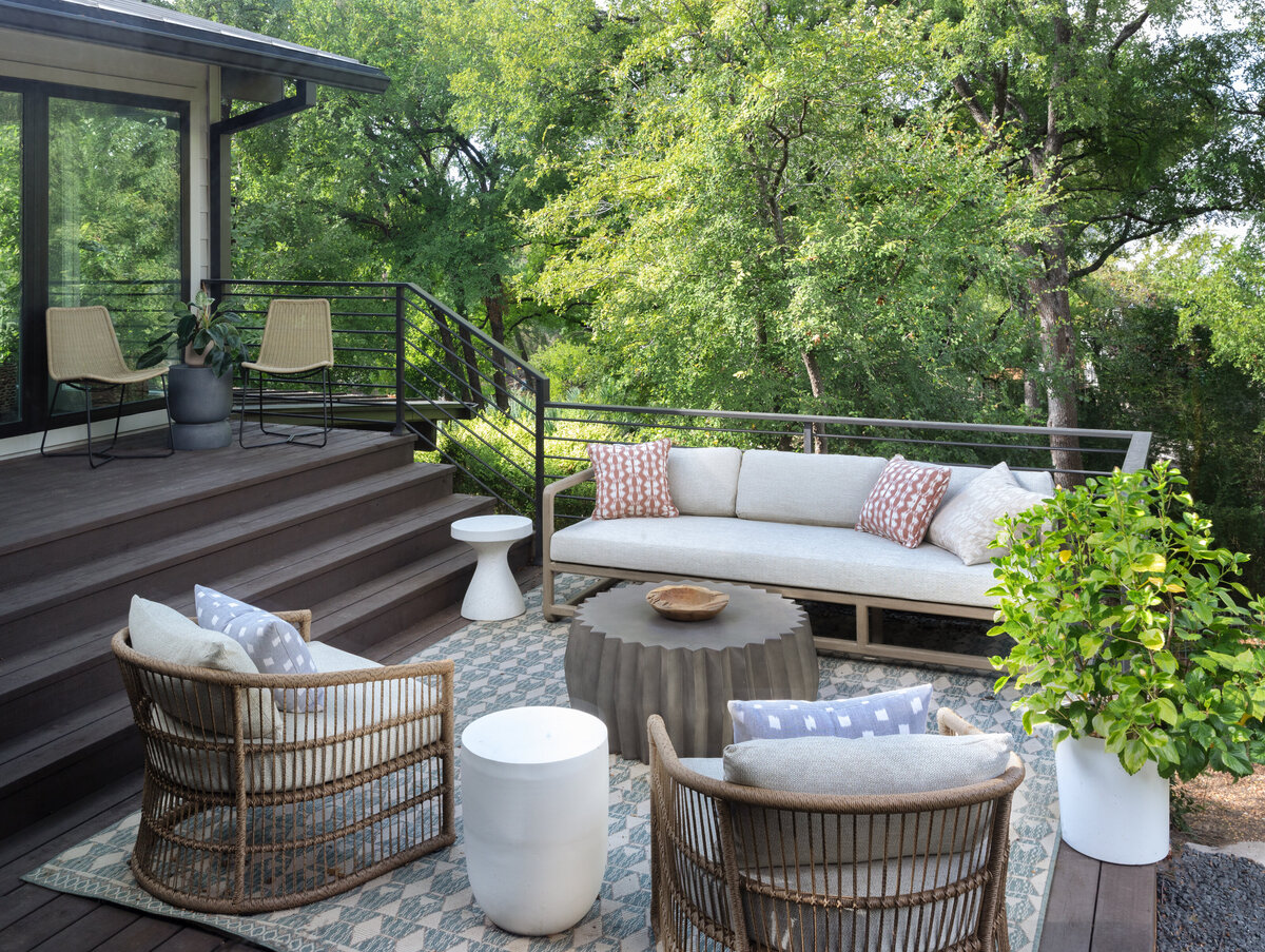 Dark comoposite deck with steps leading down to a well decorated outdoor living space with couch, chairs and a coffee table on a blue patterned rug