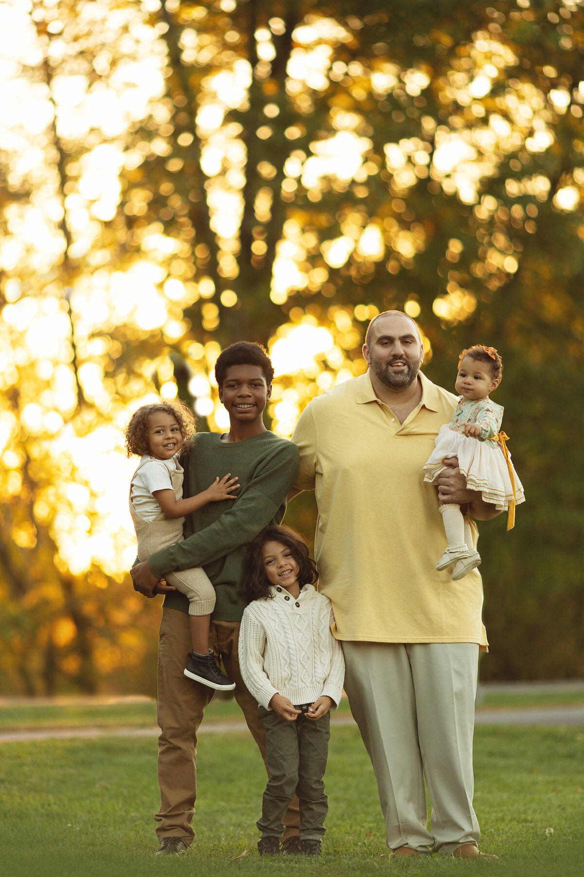 A father in a yellow shirt holds his youngest daughter  with his teen son holding another and a third toddler between them