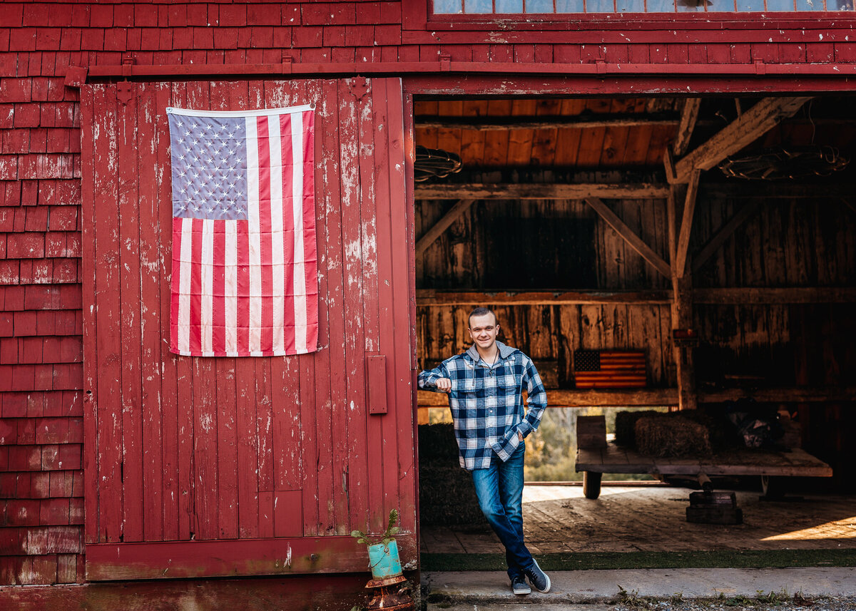 Senior photo session with guy leaning on red barn door and american flag by lisa smith photography