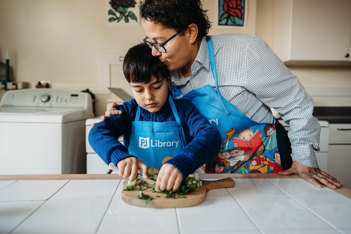 mom kisses boys head while he cuts food in kitchen