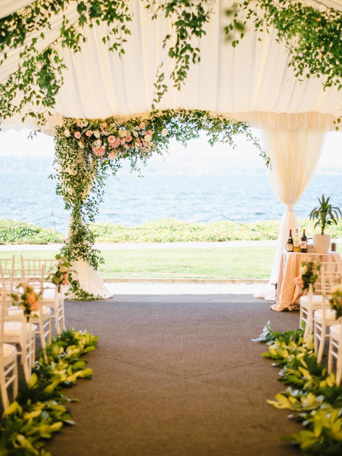 Tent wedding ceremony, green arch with pink dahlias and roses.