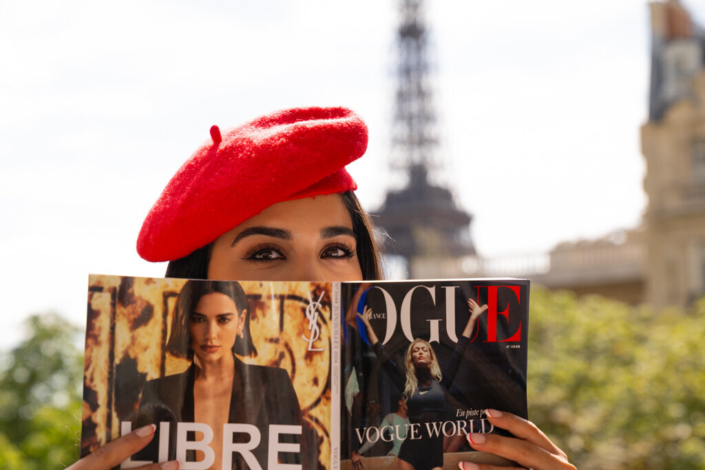 Creative Paris portrait with woman holding Vogue magazine wearing red beret with soft focus Eiffel Tower