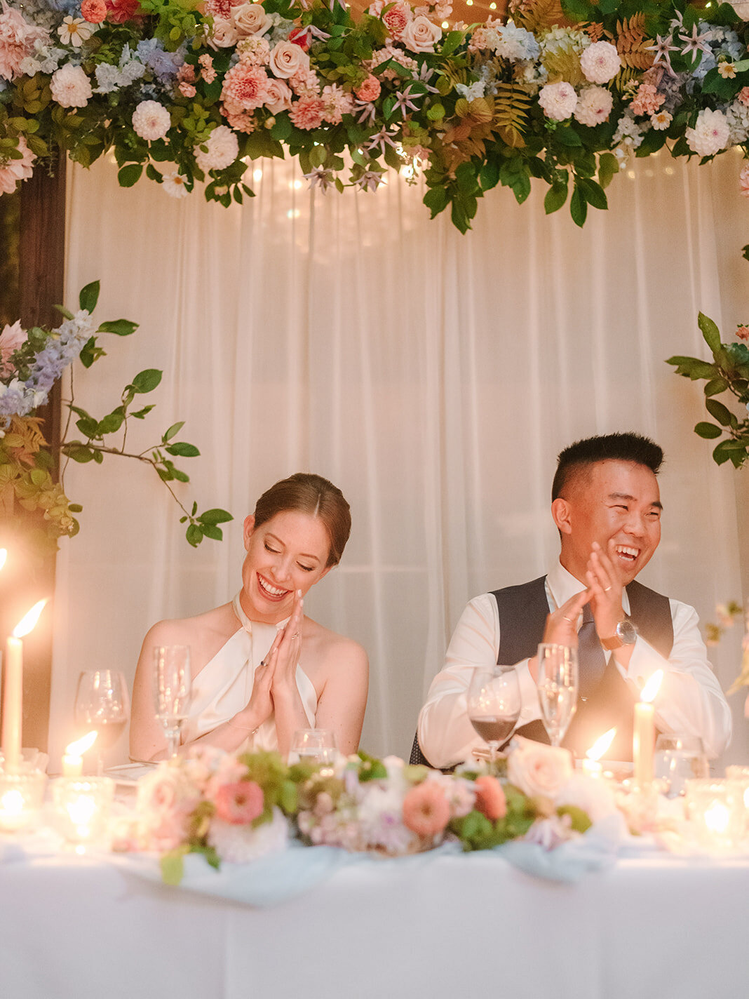 A bride and groom smile at a table at Restaurant Richmond under an arrangement of flowers.
